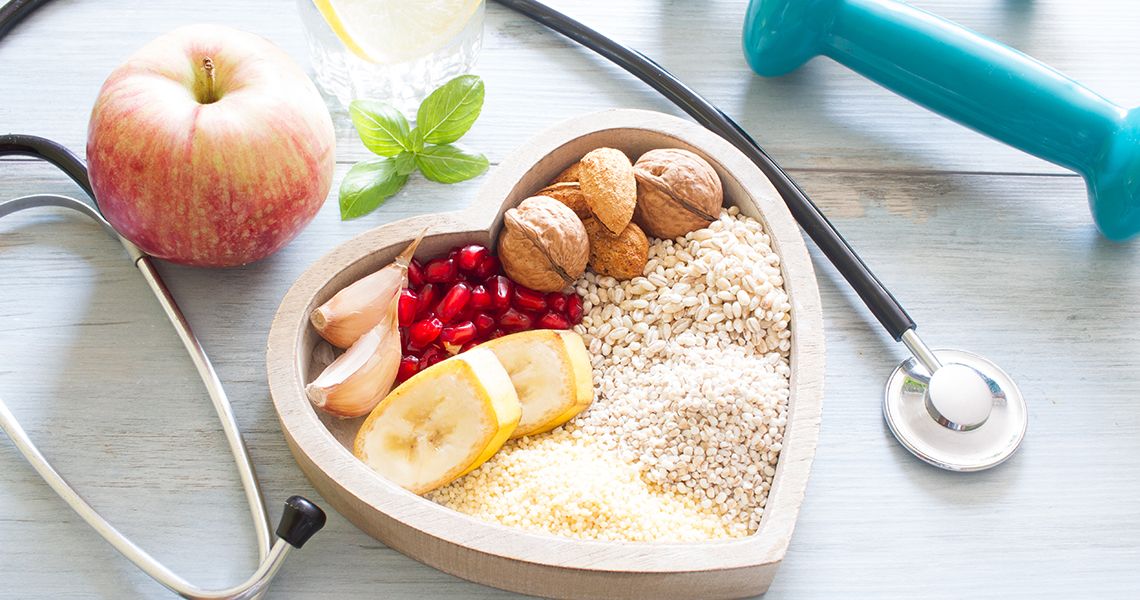 healthy food in a heart shaped bowl with a stethoscope around it, an apple, and a dumbell